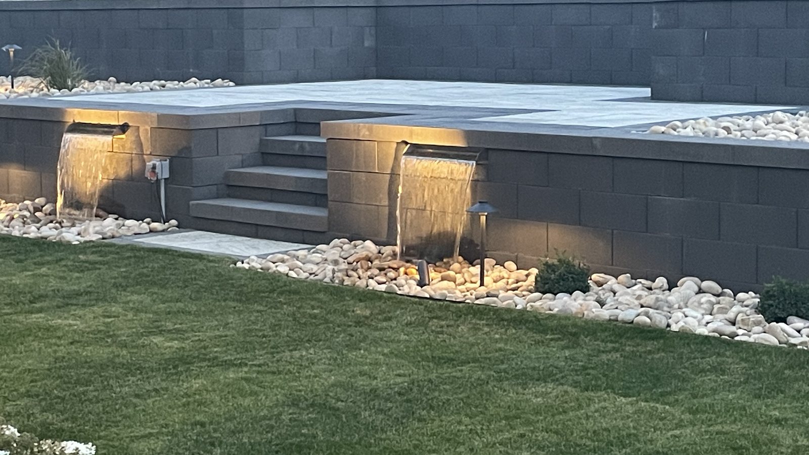 Two-tier block retaining wall with steps, water features and landscape lighting, built by Creative Edge Outdoor Living